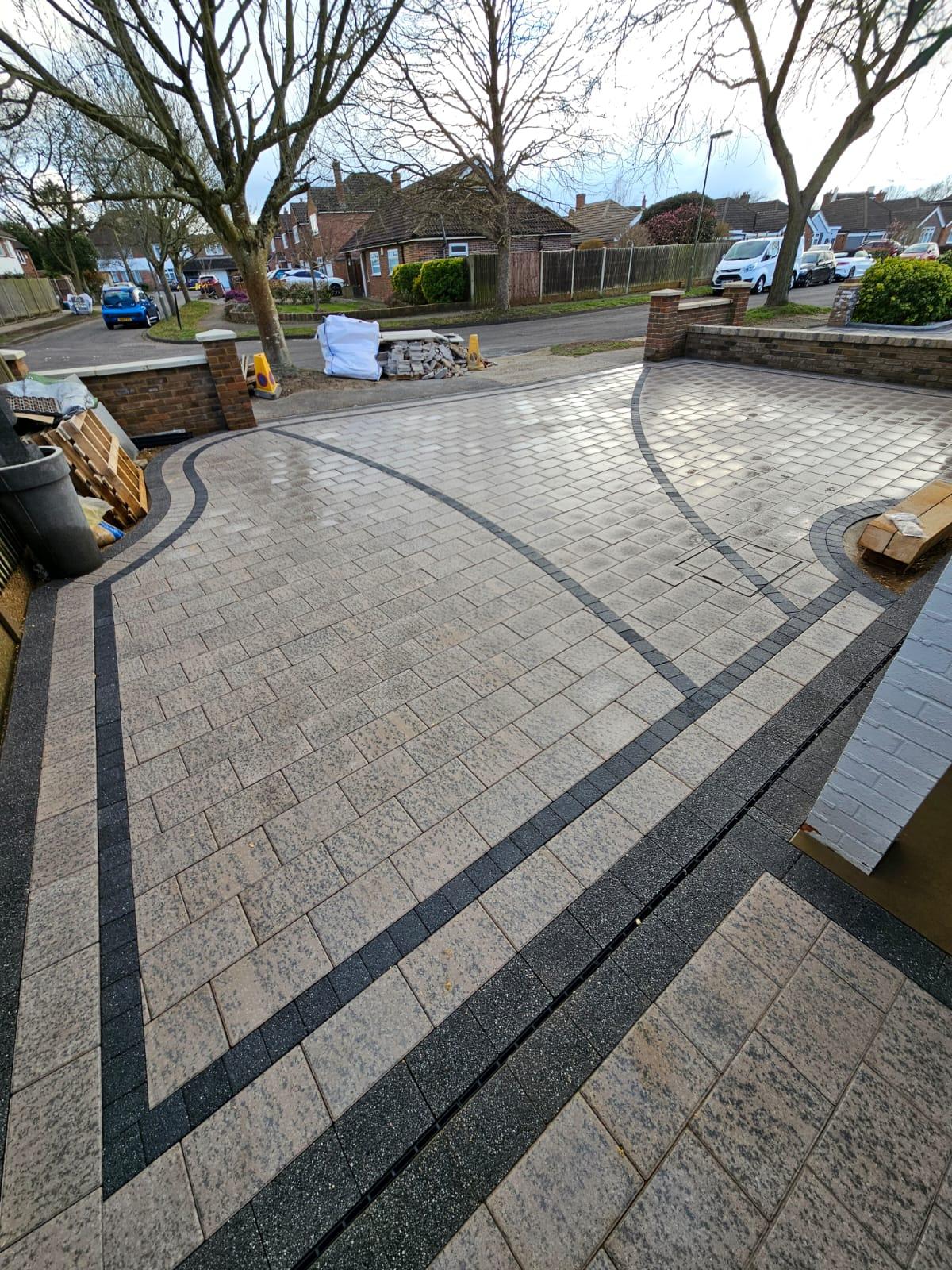 The driveway features an elegant design with interlocking pavers, providing a smooth and durable surface for vehicles. Lush greenery and colorful flowers border the driveway, enhancing its aesthetic appeal and blending harmoniously with the surrounding natural environment.