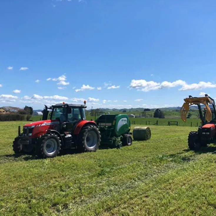  Tractor baling hay in lush Waikato hillside paddock under cloudy sky
