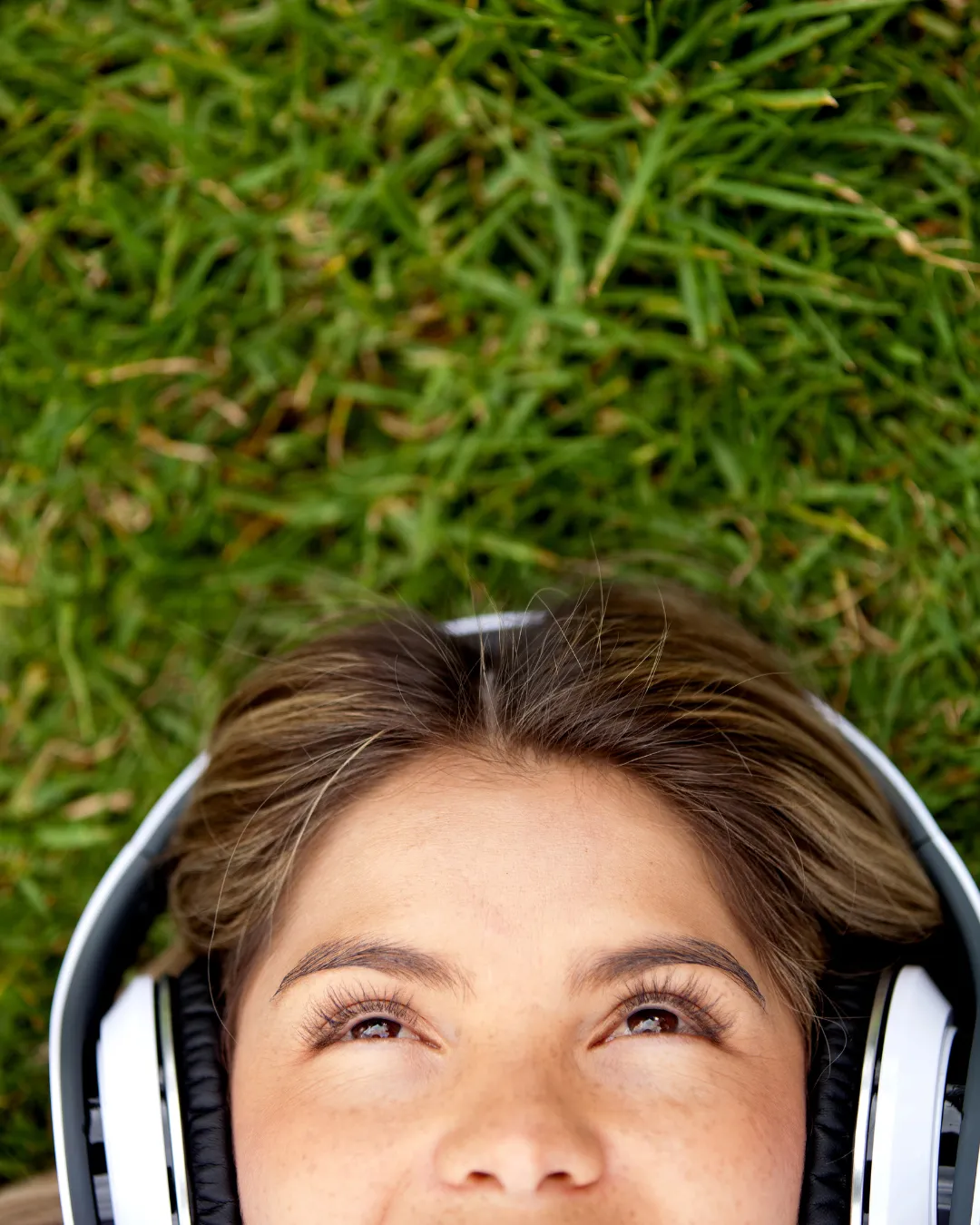 A pregnant woman lies on the grass, she has headphones on and is smiling