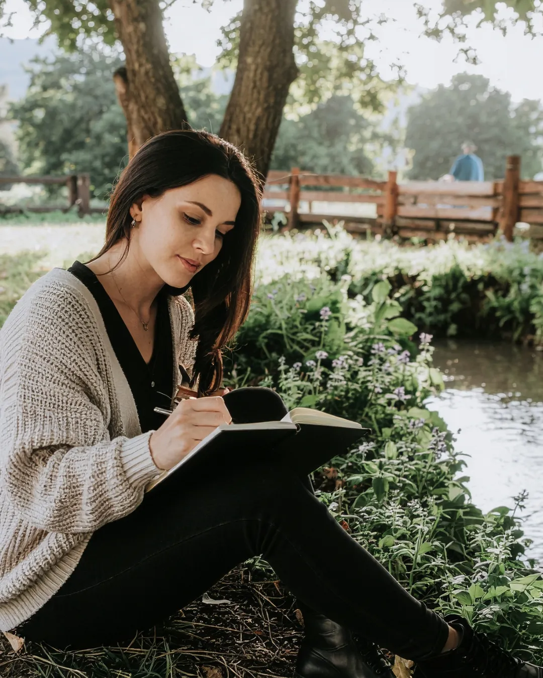 A pregant woman sits in nature, journalling.