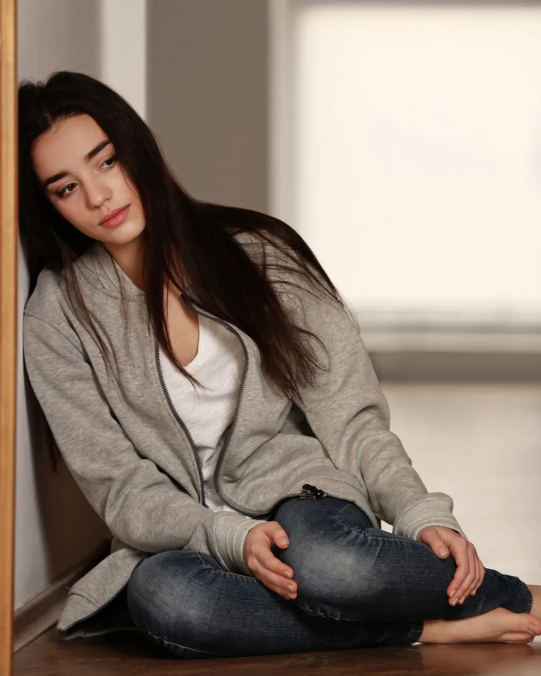 Woman sitting on floor, leaning against door, looks sad and close to tears