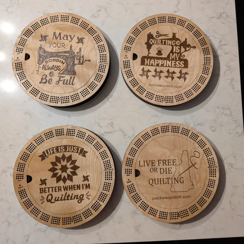Alt: Four circular laser-engraved wooden cribbage boards, each featuring a different custom quilting-themed quote and graphic