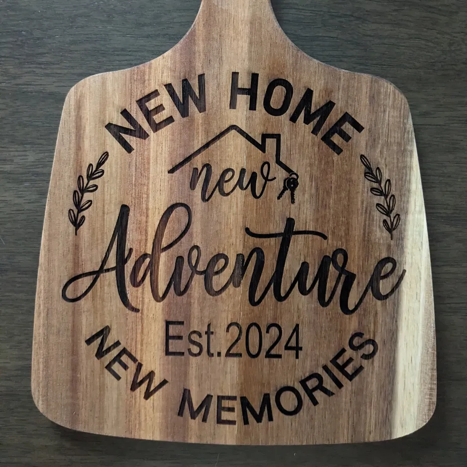 Custom laser-engraved wooden cutting board reading New Home, New Adventure, New Memories