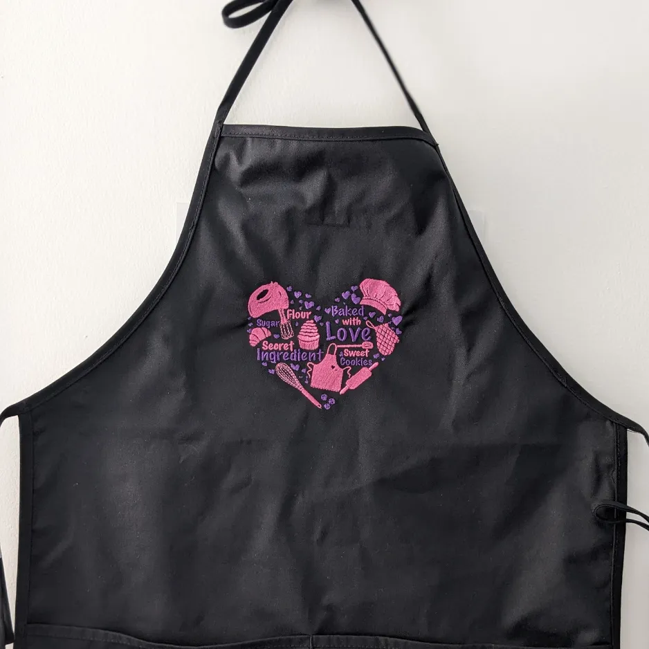 Black apron with pink heart-shaped embroidered design.