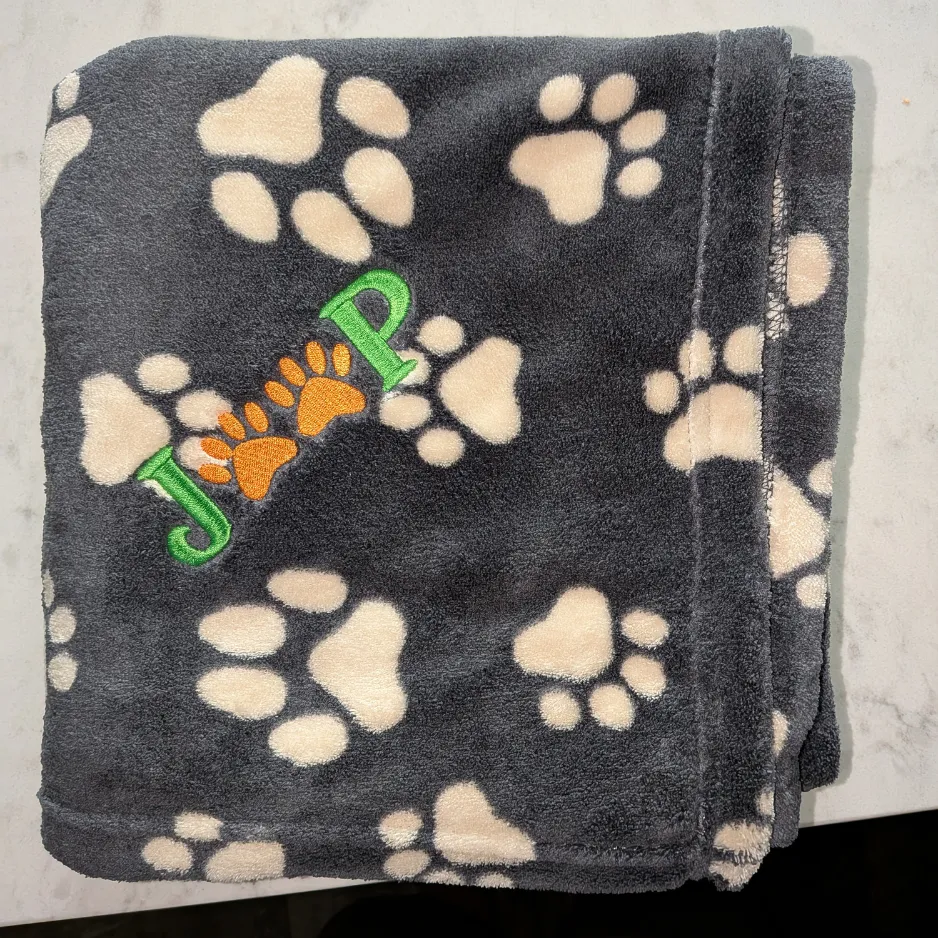 Custom embroidered gray fleece blanket with a white paw print pattern and personalized green lettering