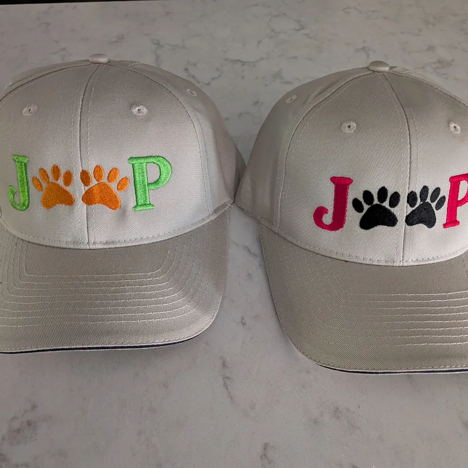 Two custom embroidered baseball caps featuring personalized names and paw print designs