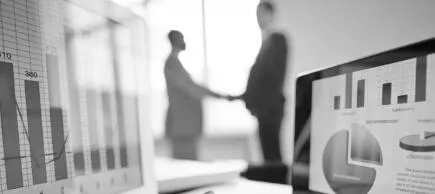 Blurry image of two business people shaking hands with reports showing in the foreground