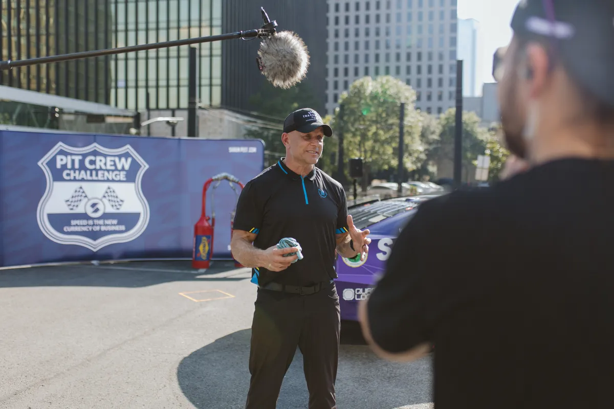 **Alt text:** NASCAR pit crew professional explaining high-performance teamwork during a Pit Crew Challenge event, illustrating lessons organizations can apply to build a high-performance culture.