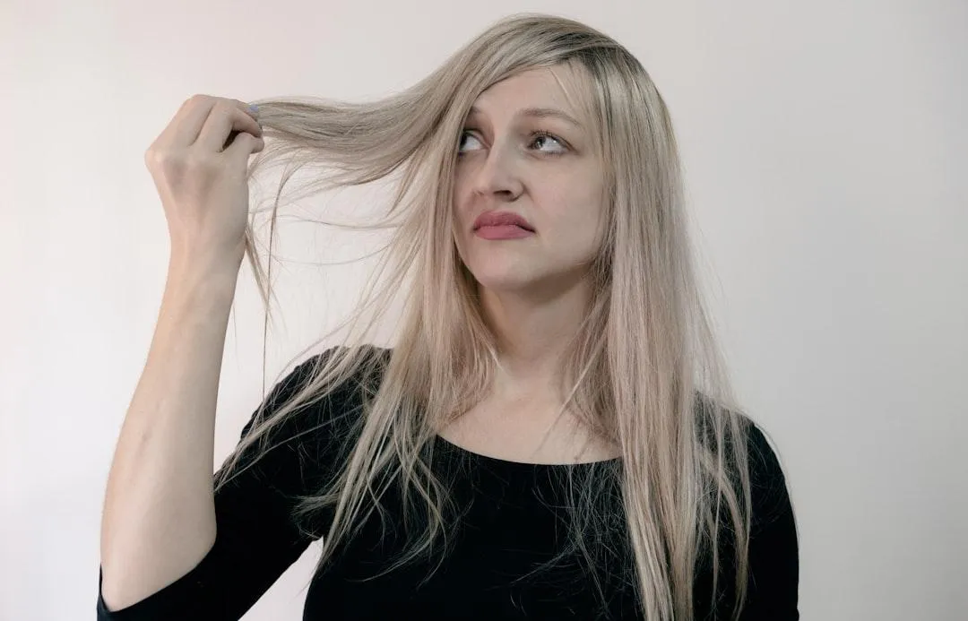 A woman with long blonde hair looking frustrated while holding a section of her thinning hair.