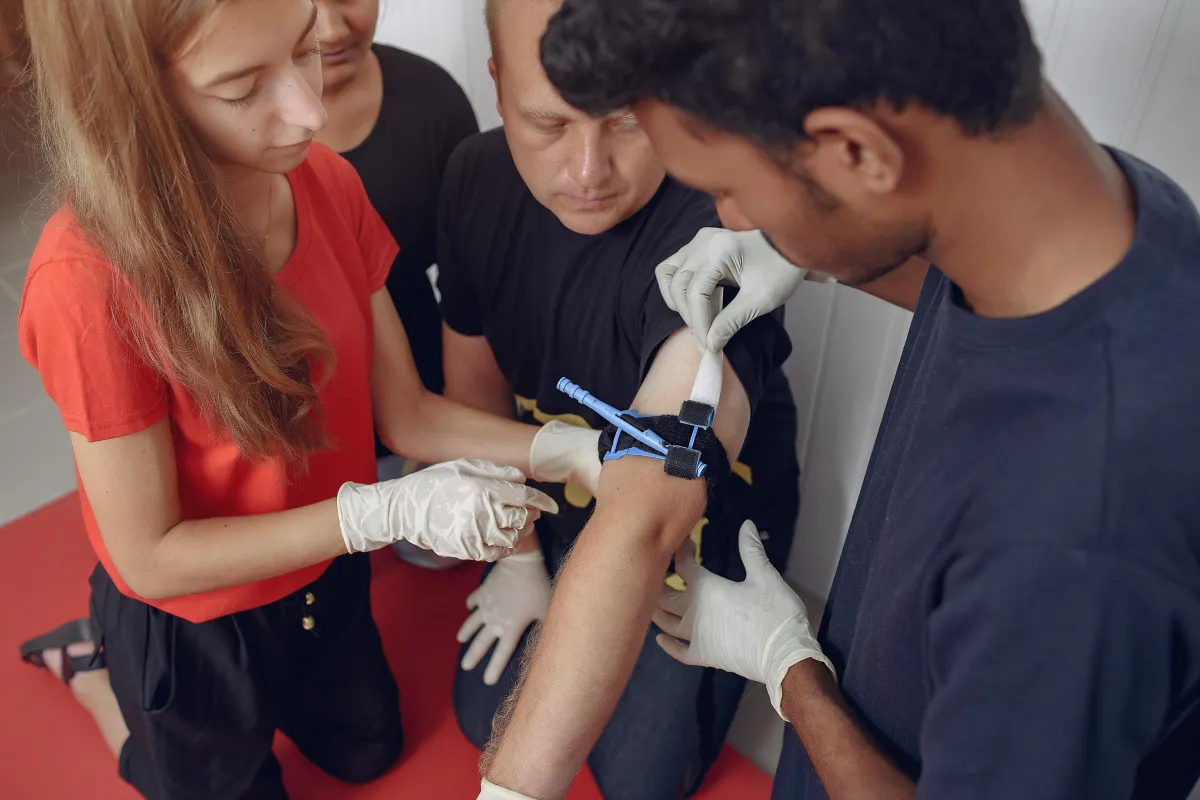 Medical students practicing blood draw procedure on patient’s arm using gloves and tourniquet