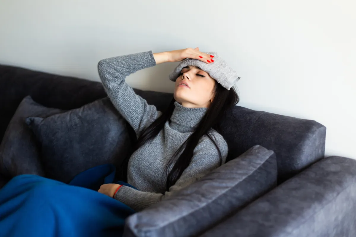 Young woman lying on couch with cold compress on forehead suffering from headache or fever