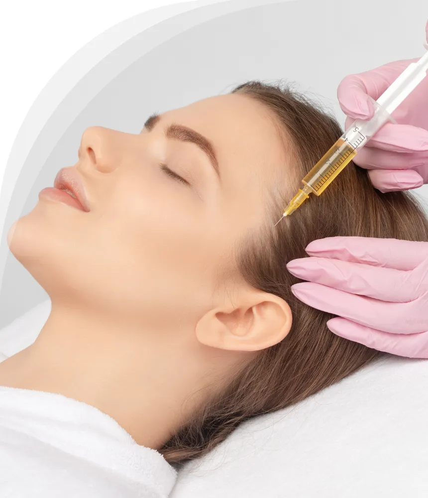 A woman with closed eyes lying down while a medical professional wearing pink gloves injects a treatment into her scalp near the hairline.