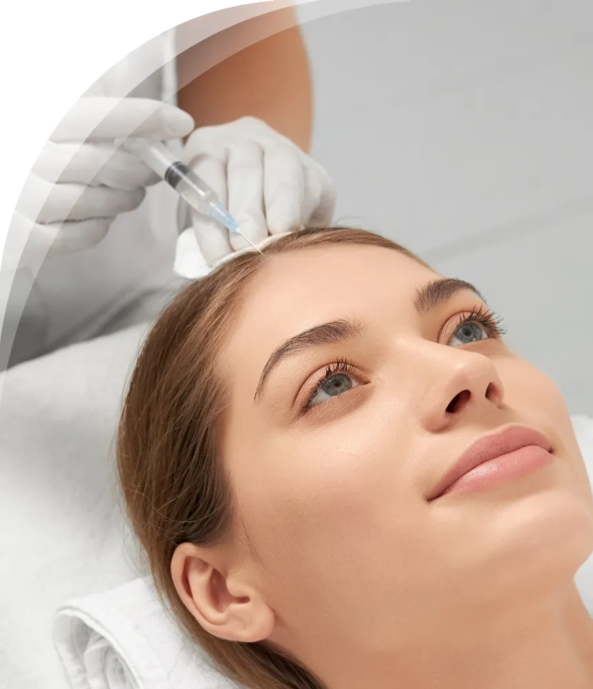 A young woman lying down with a relaxed expression as a medical professional wearing gloves prepares to inject a treatment into her scalp.