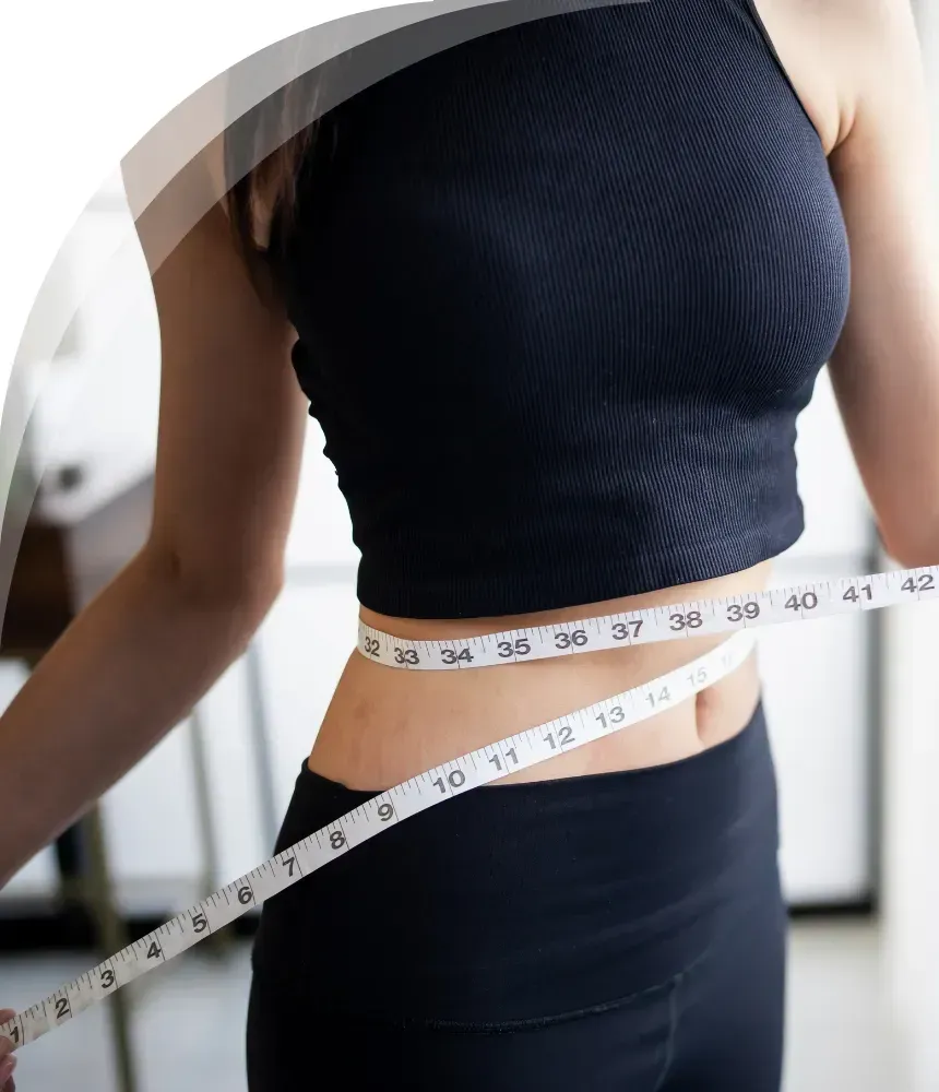 A woman wearing a black sleeveless top and black pants measuring her waist with a white measuring tape.