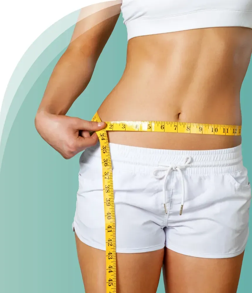 A woman wearing white shorts and a white crop top measuring her waist with a yellow measuring tape.