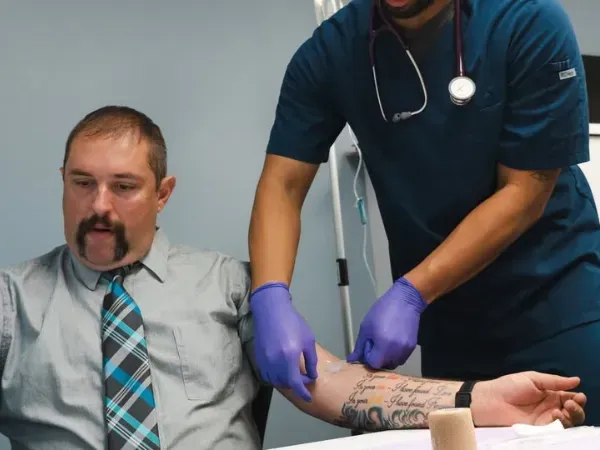 Healthcare professional preparing man with tattoos for IV therapy in medical clinic