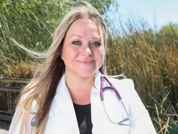 Female doctor in white coat with stethoscope smiling outdoors