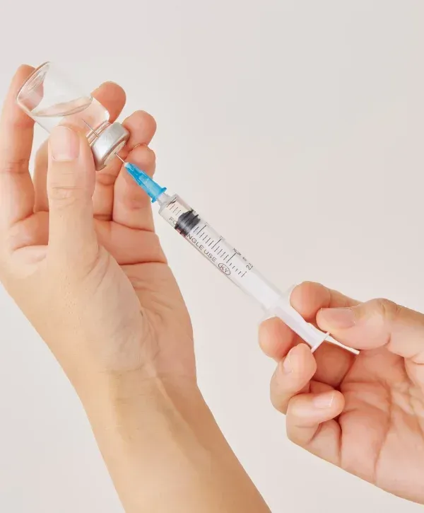 Hands drawing liquid into syringe from vial for weight loss treatment