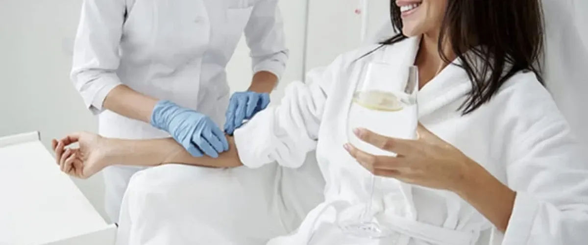 Nurse administering IV therapy to a smiling woman holding a glass of water.