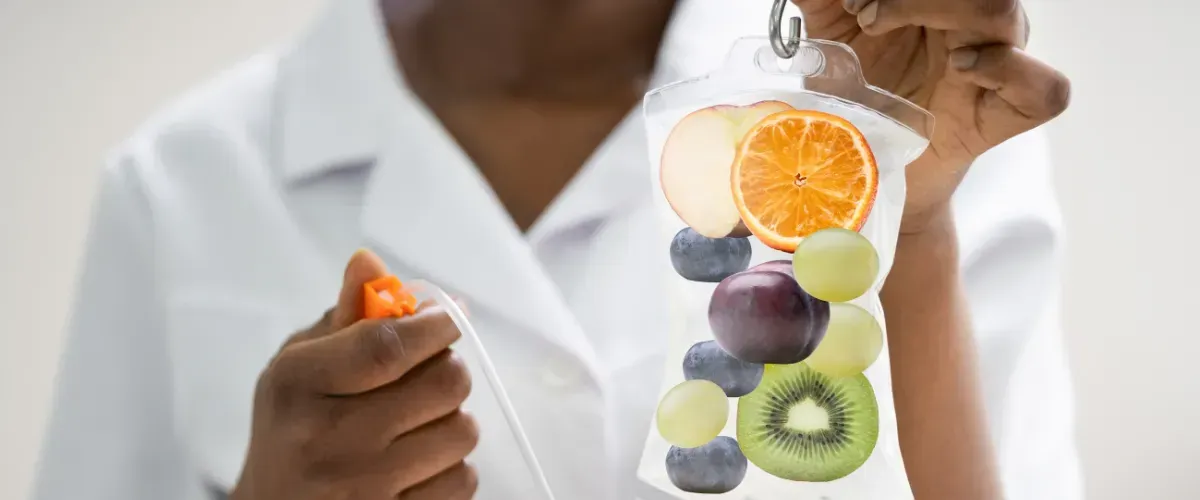 Healthcare professional holding an IV bag containing assorted fruits like oranges, grapes, blueberries, and kiwi, representing wellness and nutrition therapy.