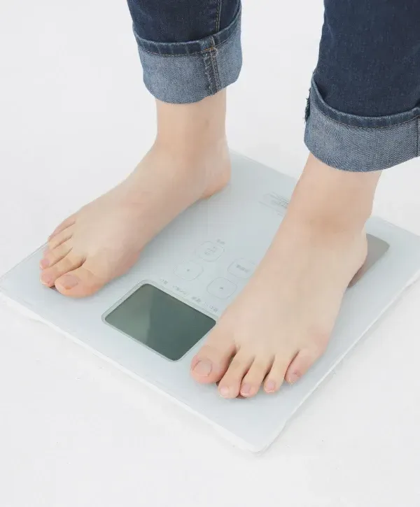 Close-up of a person standing barefoot on a digital bathroom scale to measure weight.