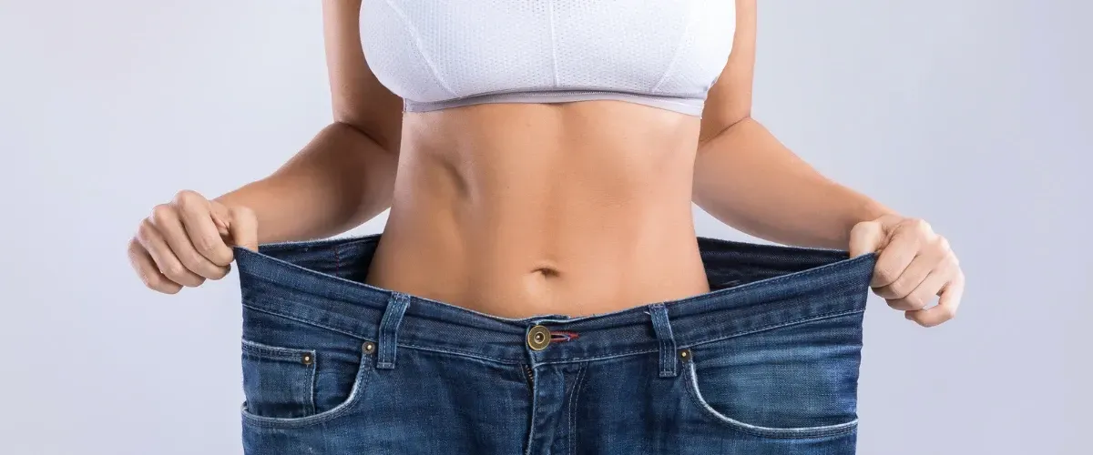 Woman showing significant weight loss by holding out oversized jeans around her waist.