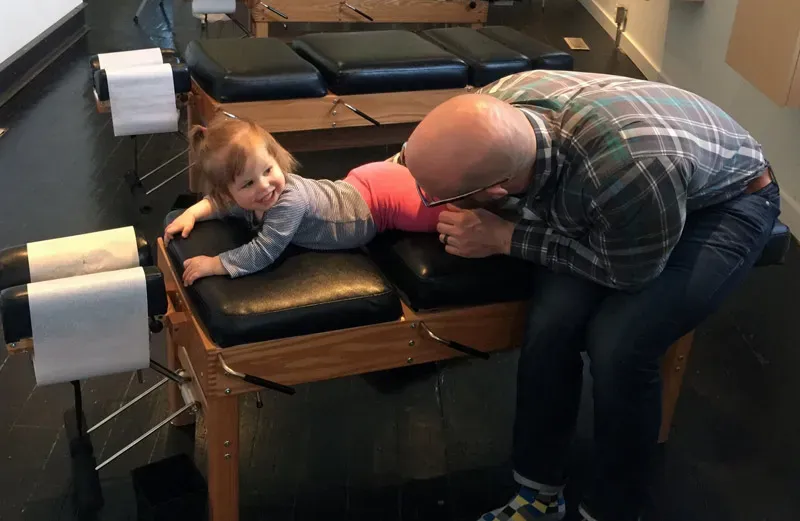 Dr. Richards gently adjusts a smiling toddler lying face down on a chiropractic table in a treatment room.
