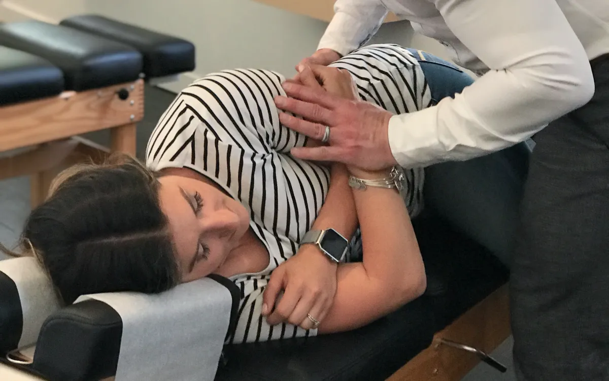 A woman lies on her side on a chiropractic adjustment table while Dr. Richards prepares to perform a spinal manipulation.