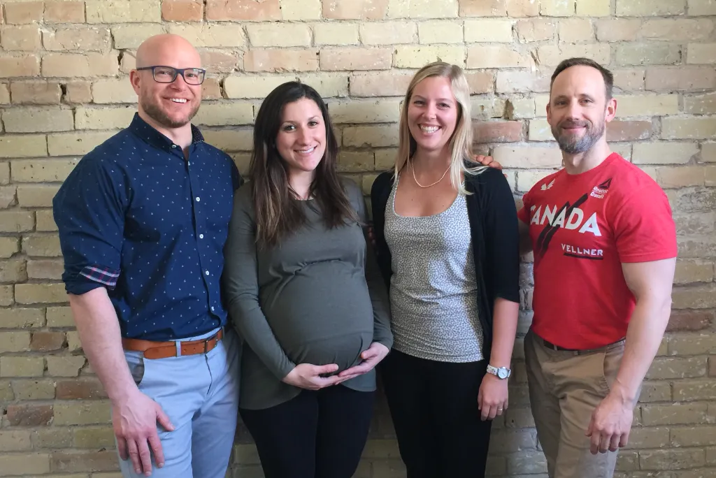 Dr. Richards stands smiling on the left with three other people, including a pregnant woman, as they pose together in front of a brick wall.