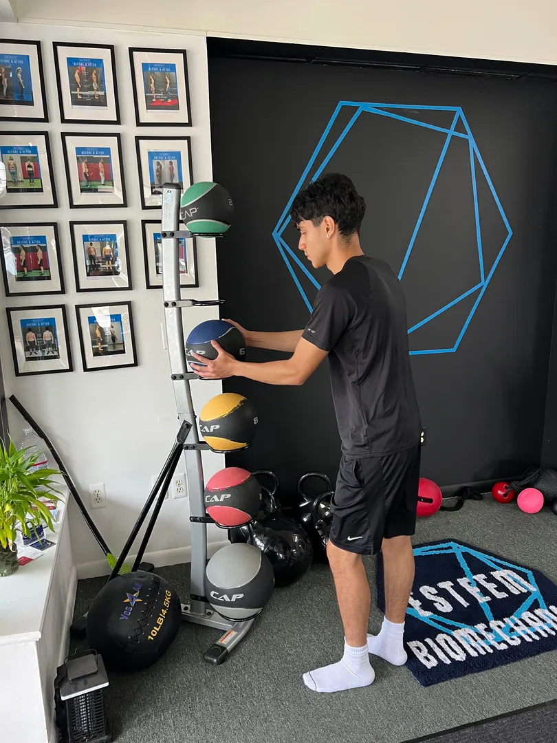 Personal trainer organizing medicine balls at Esteem Biomechanics personal training studio in Waldwick, NJ.