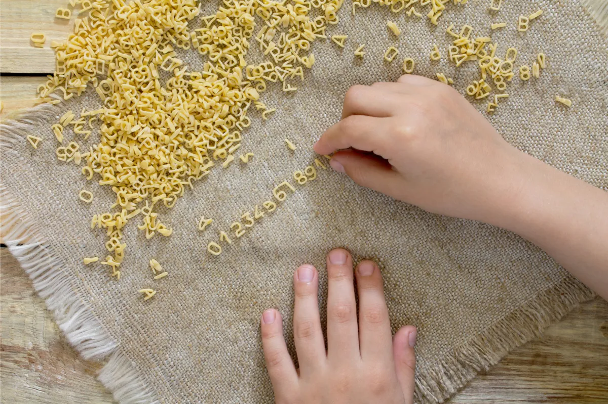 Child writes A in green sand