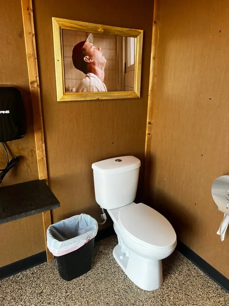 Modern, clean restroom at SOBO's Campground featuring a private toilet, sink area, rustic wood walls, and unique baseball-themed wall décor.