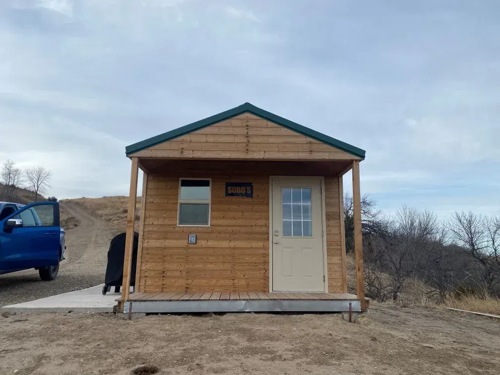 Rustic camping cabin at SOBO's Campground with covered front porch, private entrance, and peaceful Badlands surroundings.