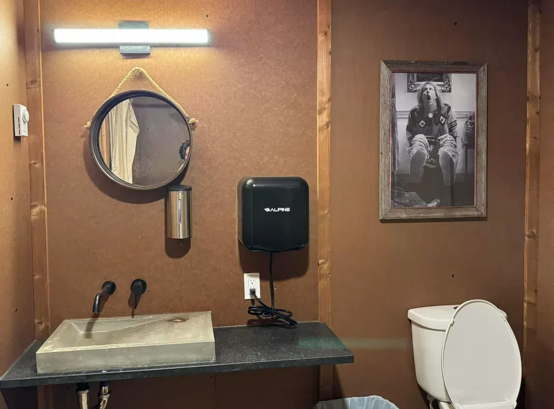 Private campground bathroom at SOBO's Campground featuring a concrete sink, modern lighting, toilet, and rustic wood interior.