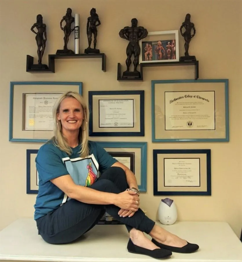 Dr. C sitting with trophies and diplomas