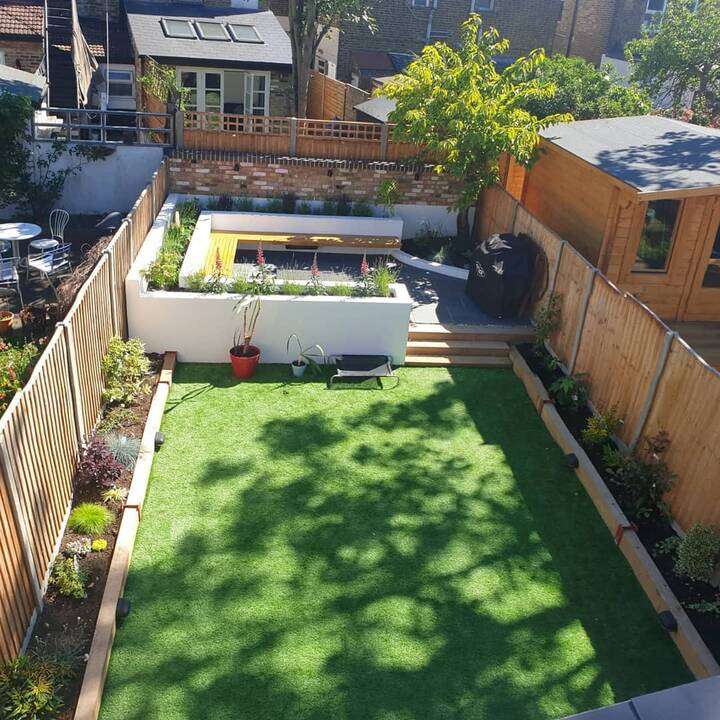 Lush rear garden lawn with curved planted border and dark fence panels in Pinner