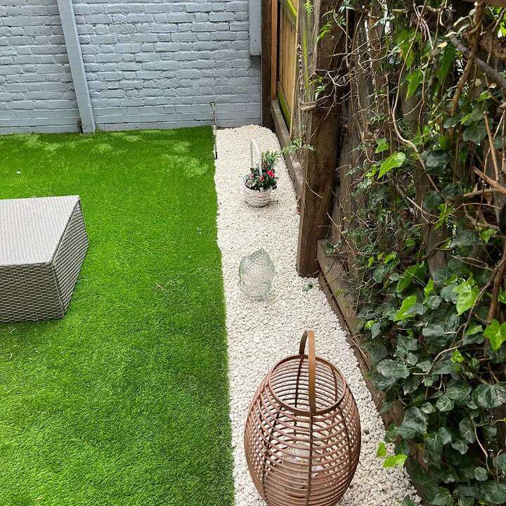 Artificial grass garden with white timber shed at the rear in Harrow