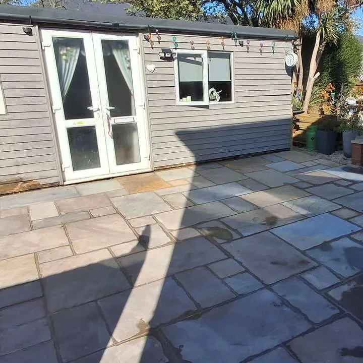 Finished natural stone patio laid in front of a timber garden room with brick raised bed in West London