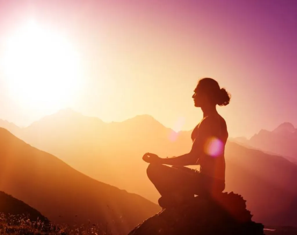 Instructor in a serene studio scene holding a folded blanket and mat, smiling warmly.