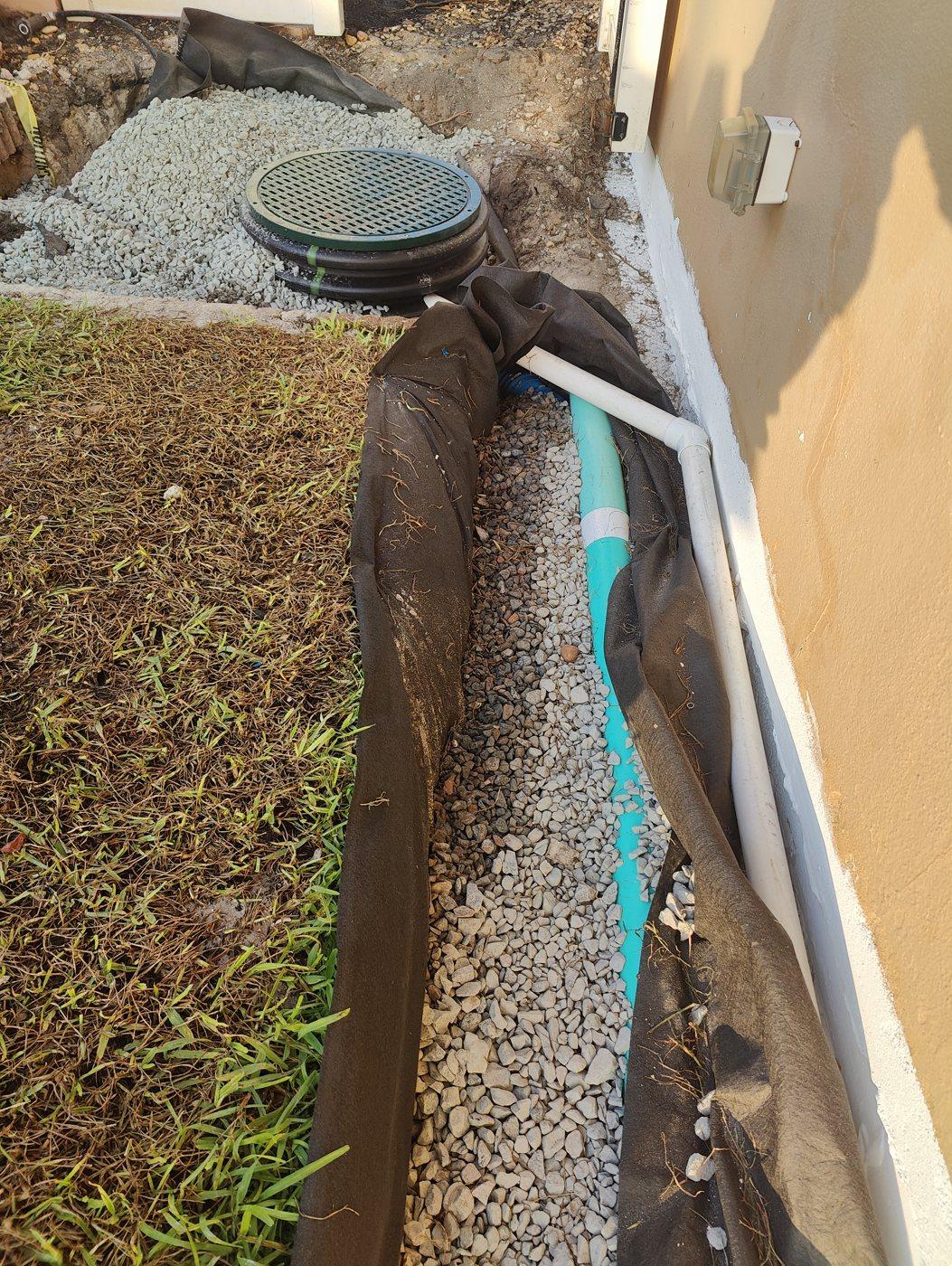Foundation drain in fabric and granite with a downspout tied in and the wall coated