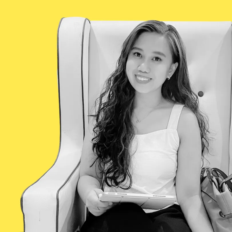 Sheim, from Sheldon Social, sits in a wingback chair, holding a tablet, smiling to camera. The background is yellow.