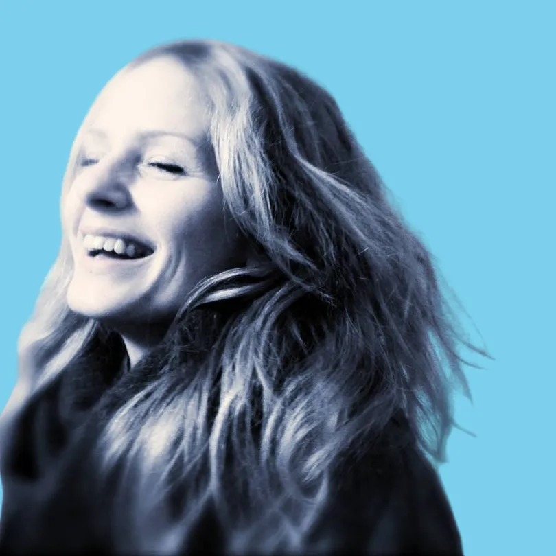 kati Harris, from Sheldon Social, on a blue background, smiles towards the camera.