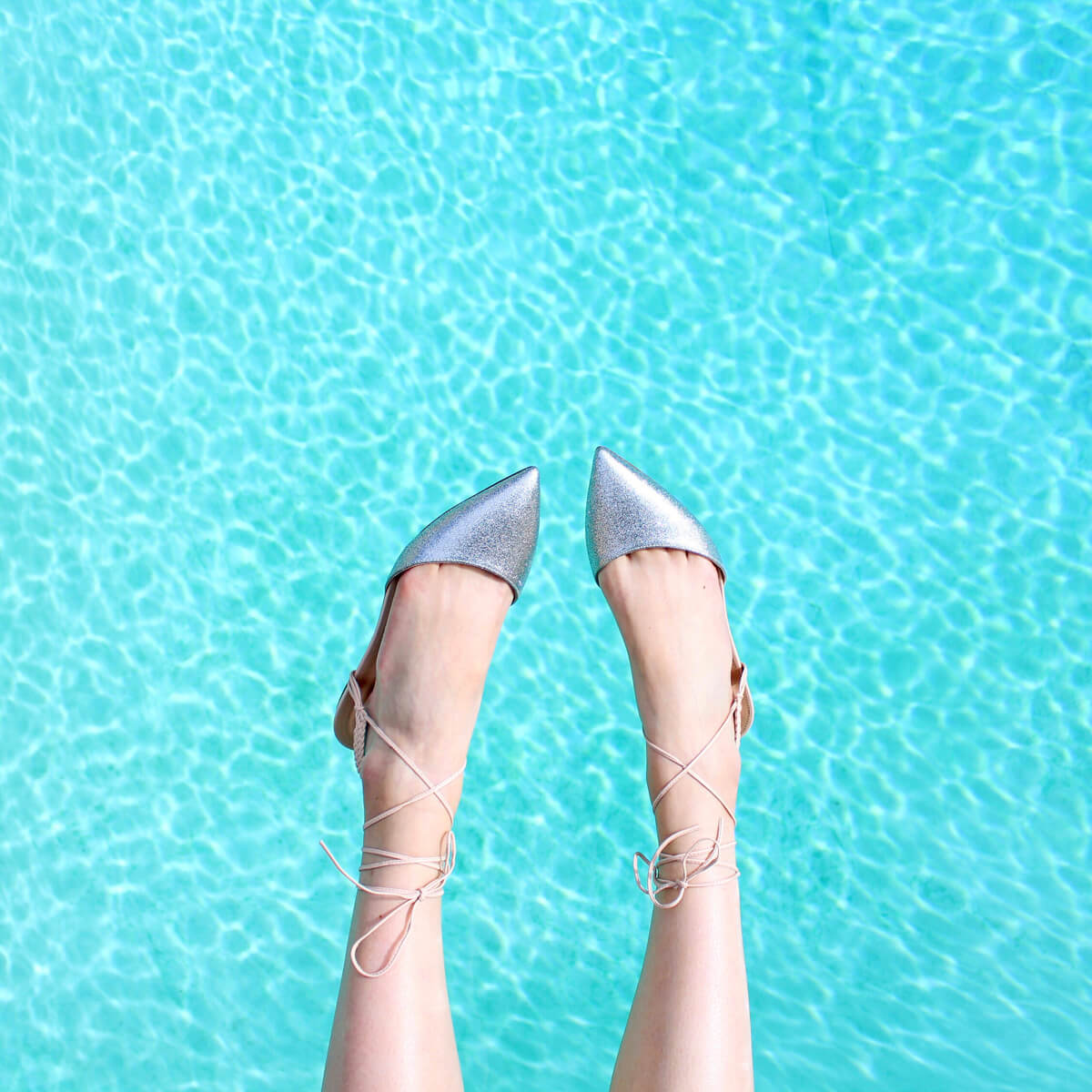 A playful flat-lay style photograph of silver lace-up shoes held up against a turquoise pool — used to illustrate a Sheldon Social article on content strategy and brand positioning.