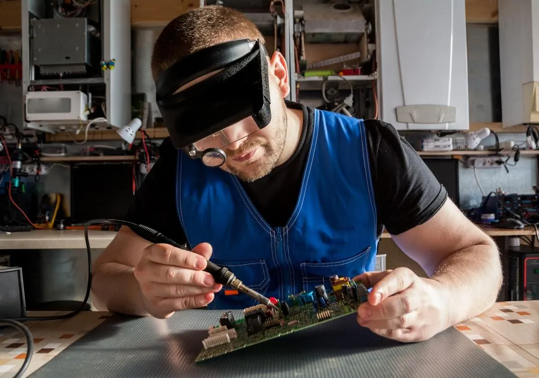 guy with black tshirt and blue vest tinkering with electrical board