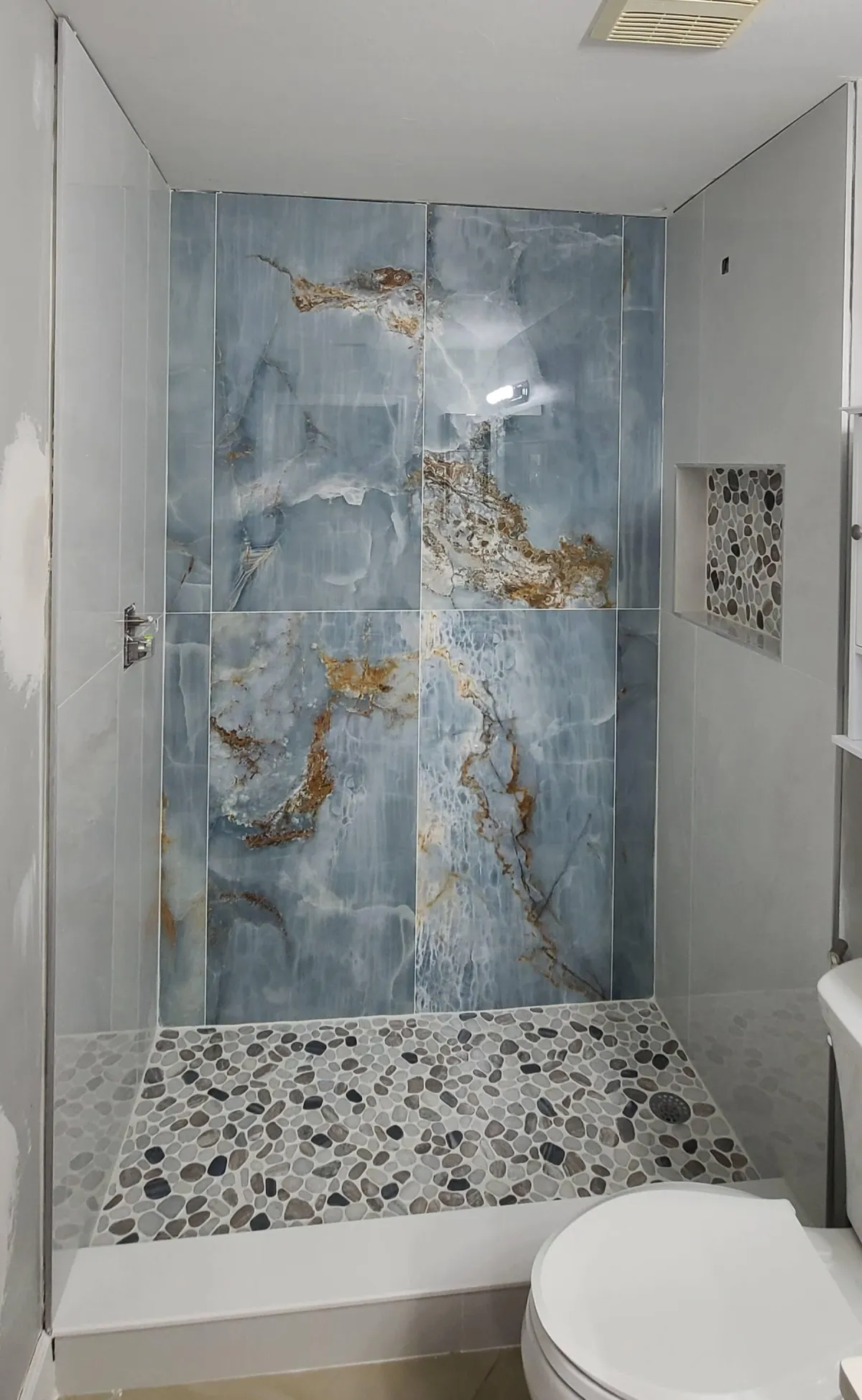 Bathroom shower with large blue onyx-style tiles, natural veining, and pebble stone flooring for a spa-inspired look.