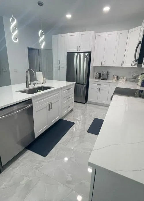 Bright contemporary kitchen featuring a large island sink, quartz countertops, white shaker cabinets, and high-gloss floor tiles.