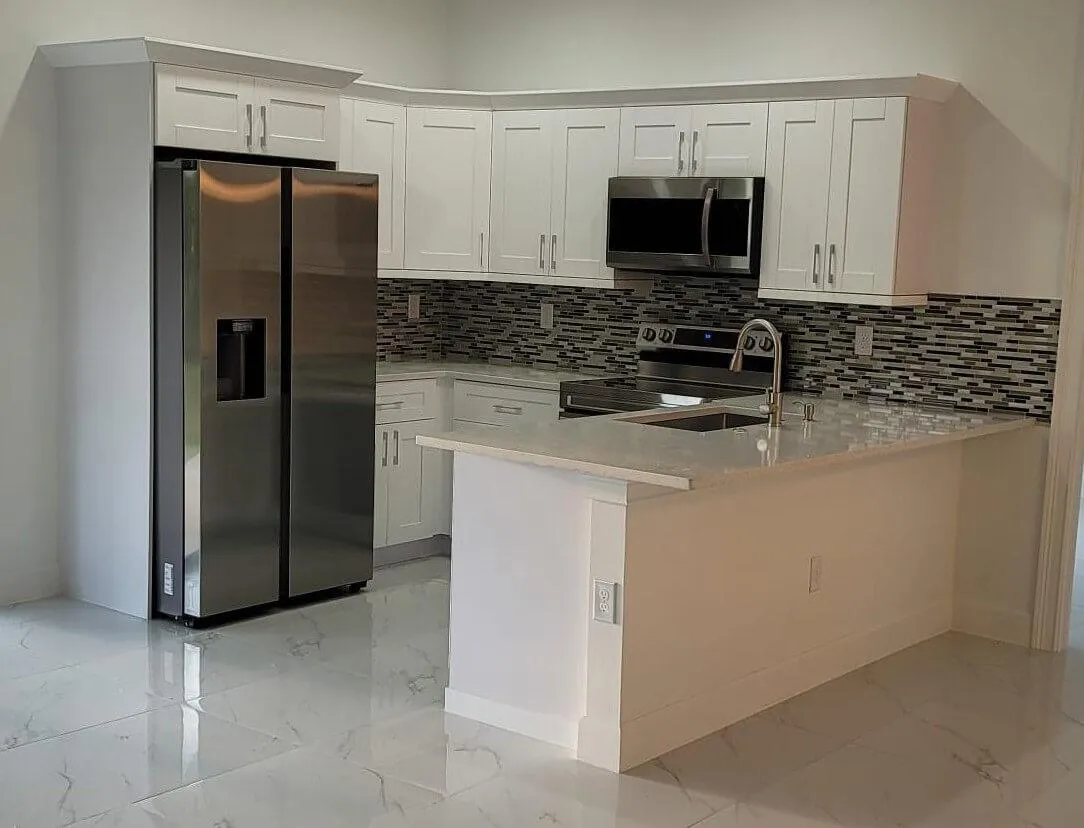 Compact modern kitchen with white shaker cabinets, stainless steel appliances, mosaic tile backsplash, and quartz countertops with peninsula.