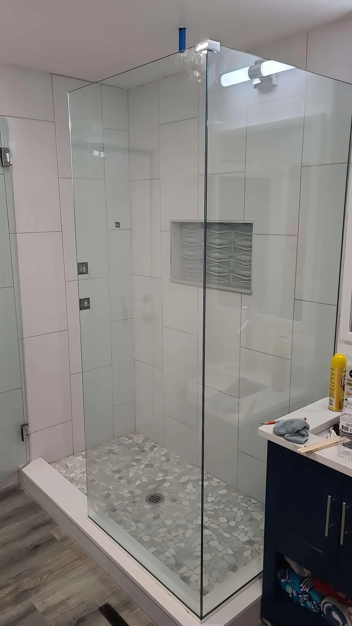Frameless glass shower with large white tiles, built-in niche, and pebble stone shower floor in a modern bathroom remodel.