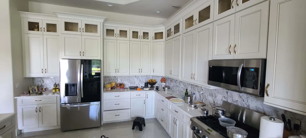 Spacious kitchen remodel featuring tall white shaker cabinets with gold hardware, stainless steel appliances, and a textured marble backsplash.