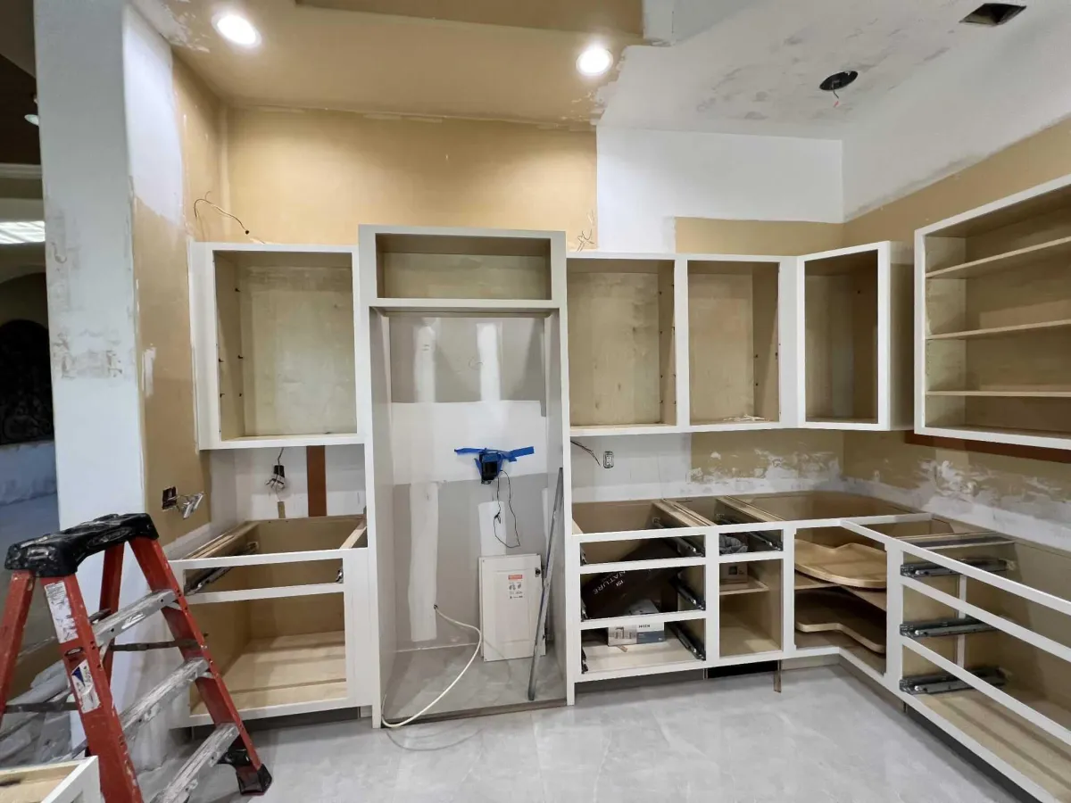 Kitchen remodeling in progress showing custom cabinet installation, open-frame storage layout, and prepped drywall awaiting paint and finish.